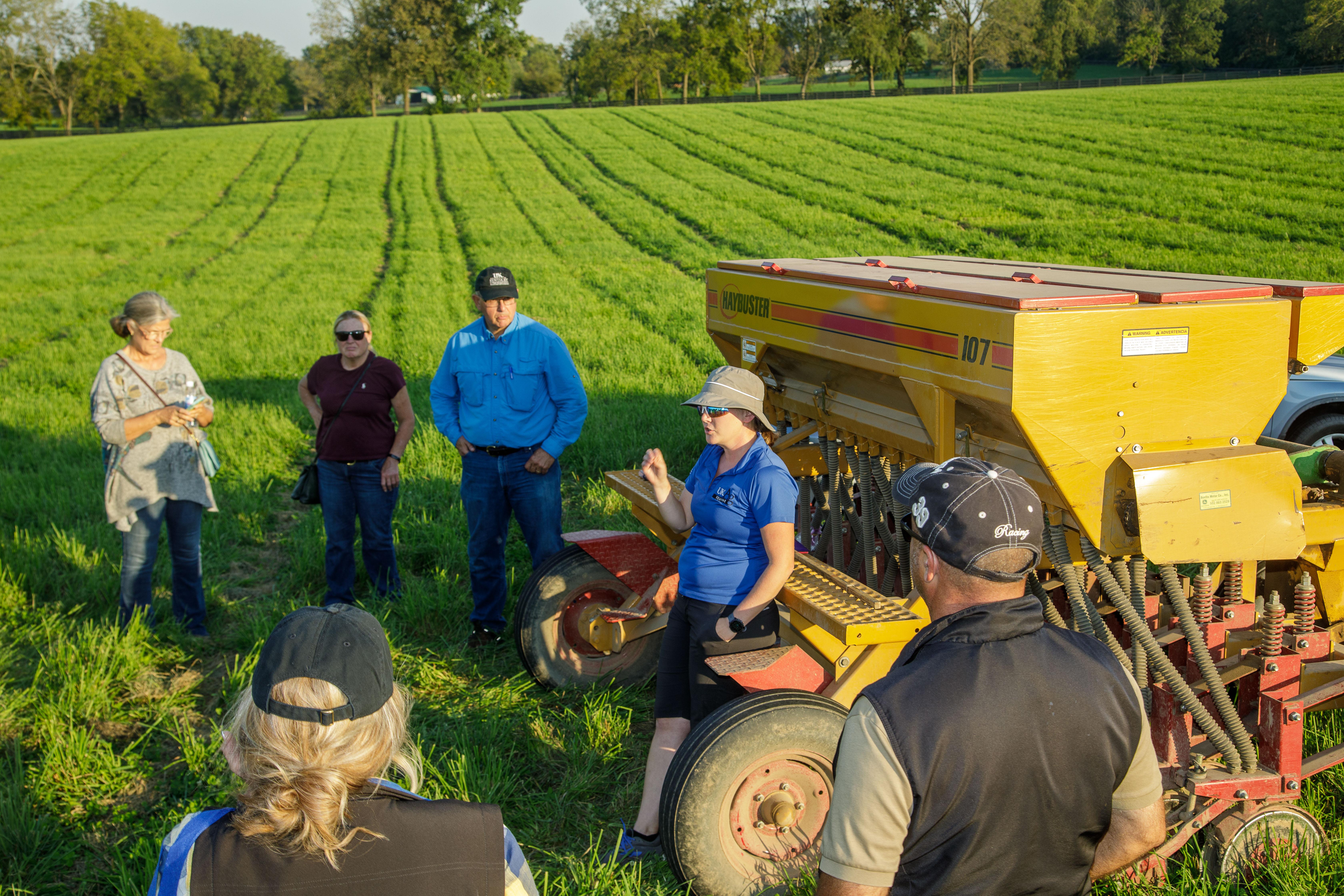 People stand in a field talking next to farm equipment